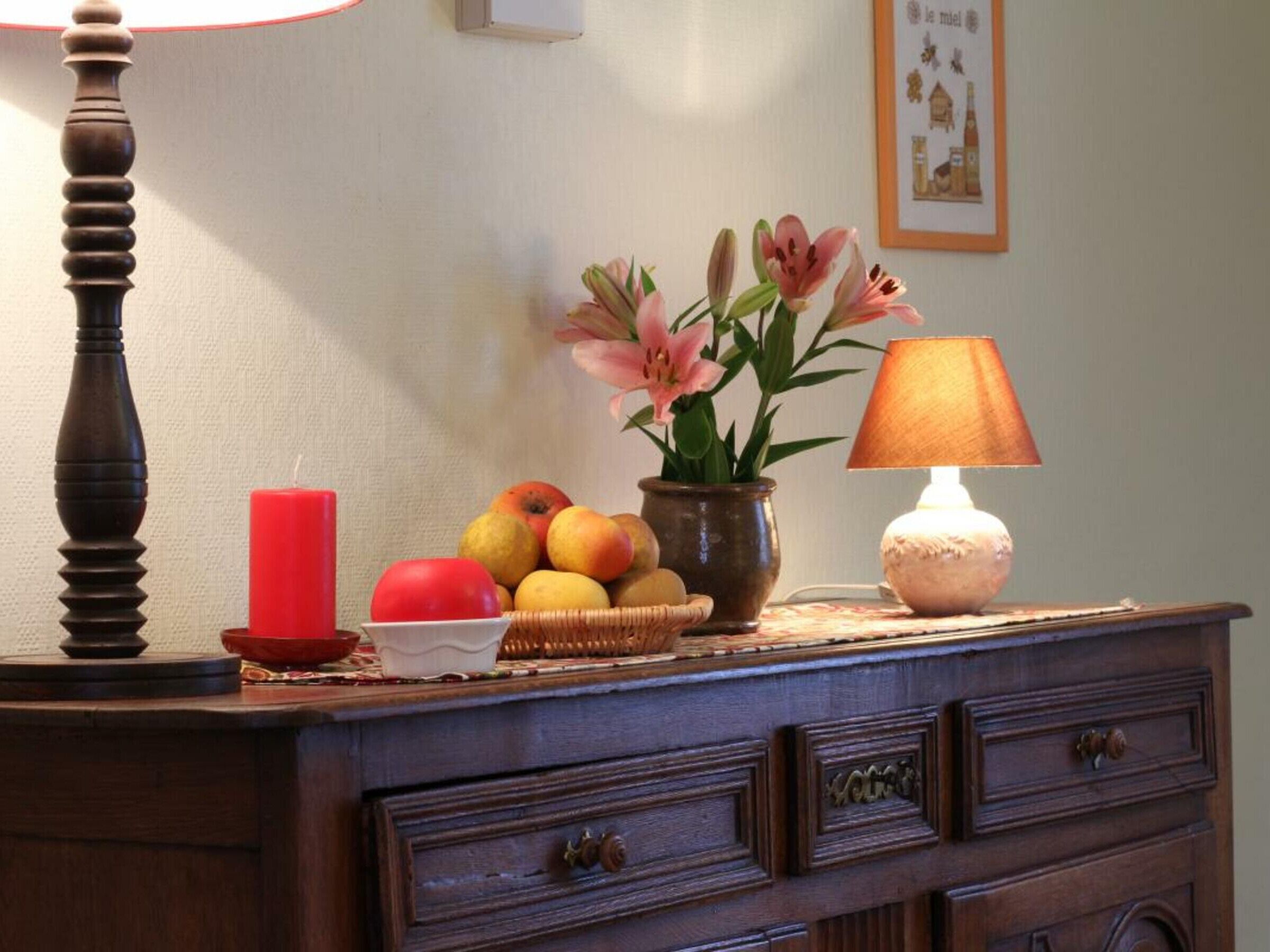 Une commode en bois, une bougie rouge, un bol de fruits et un vase rempli de fleurs.