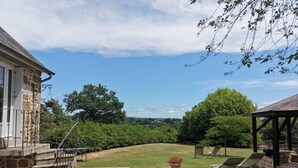 A stone house with a paved patio, a covered seating area, and a view of a grassy yard with trees. - Charming house with garden, high speed, near Bagnoles de l'Orne (Antoigny)