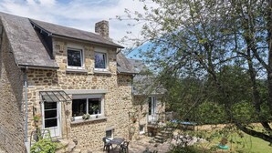 A stone house with a patio, a chimney, and a view of the surrounding landscape. - Charming house with garden, high speed, near Bagnoles de l'Orne (Antoigny)