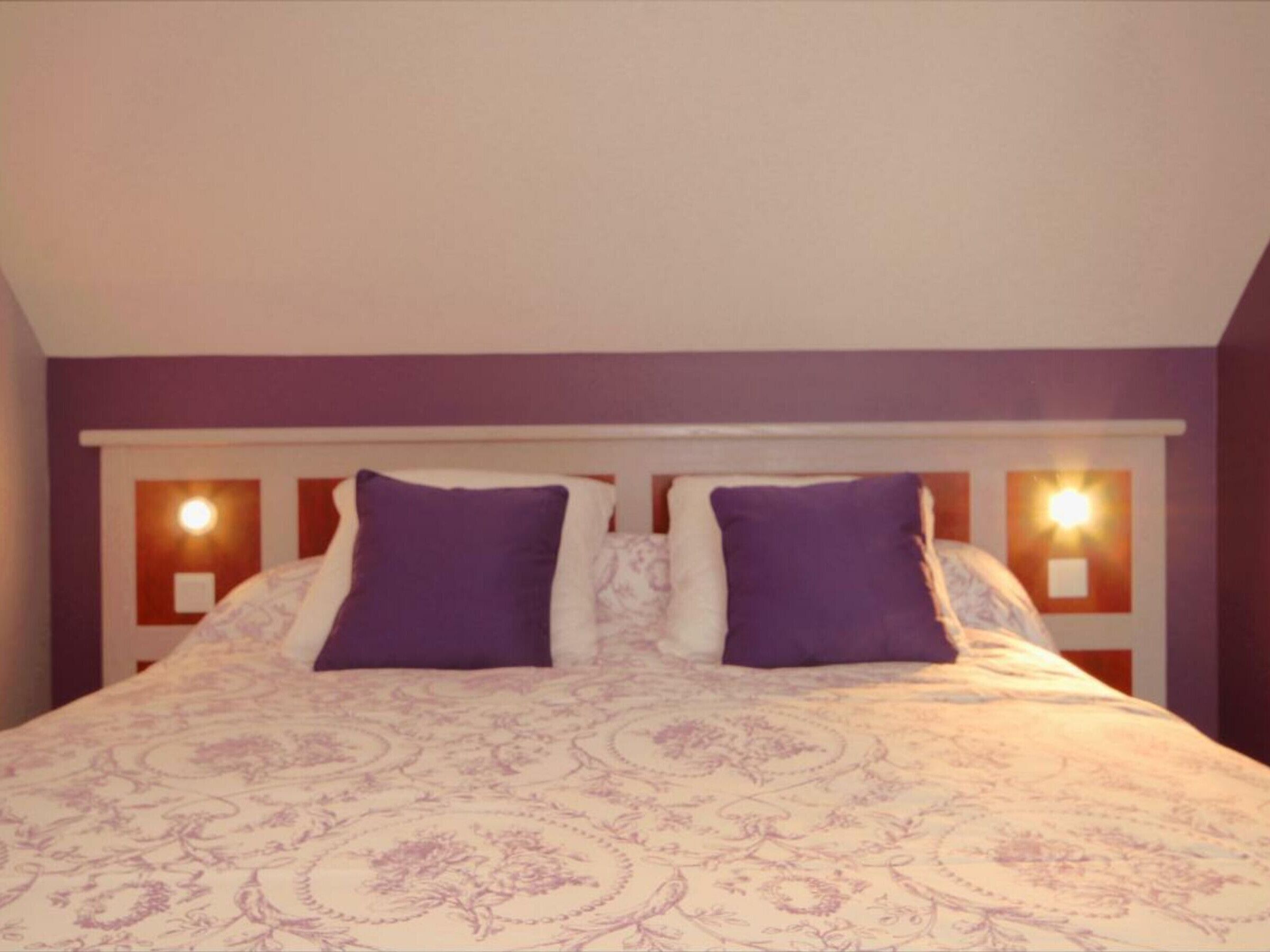 Une chambre à coucher avec un lit, des oreillers violets et des lampes fixées au mur.