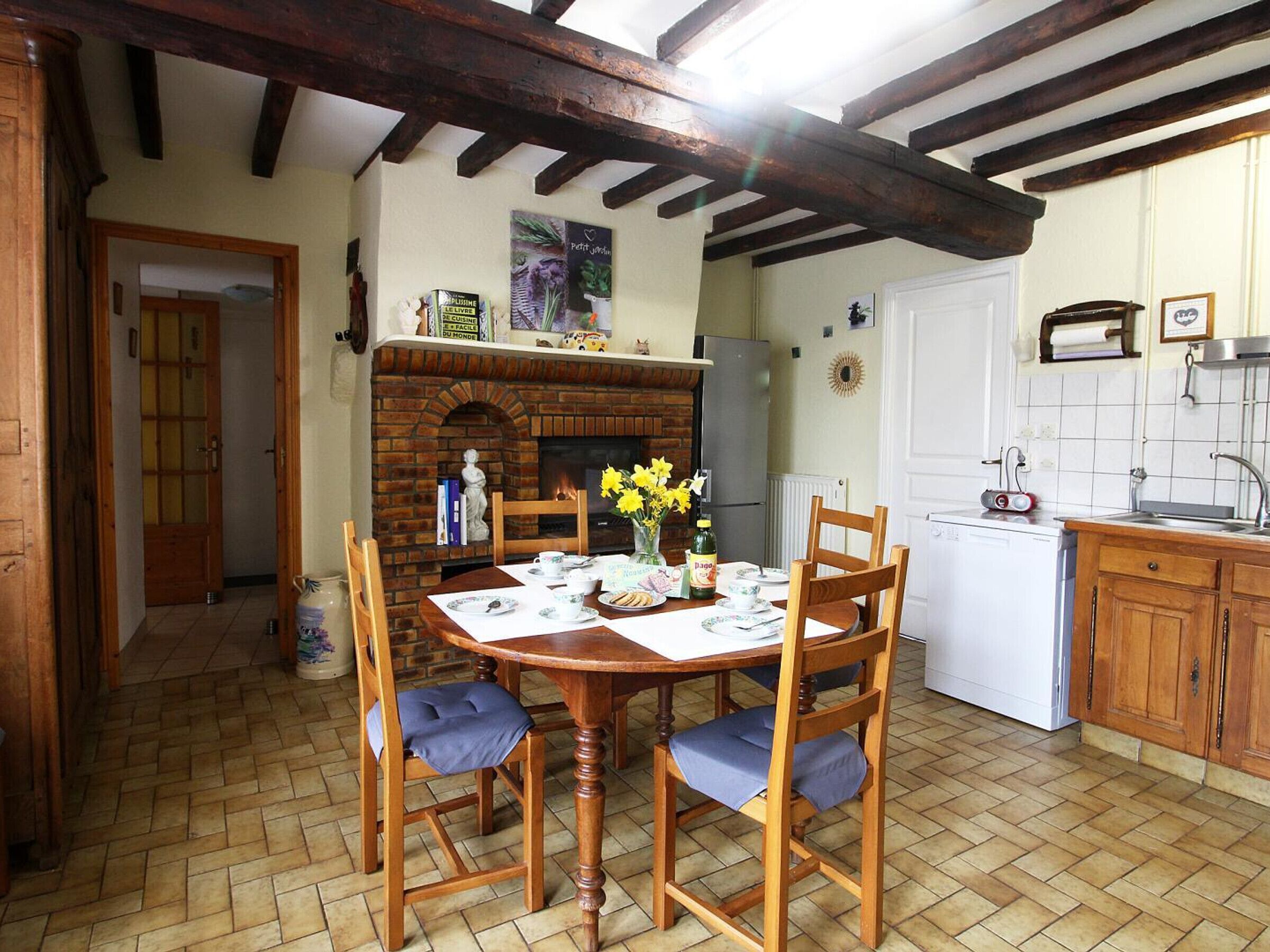 A cozy kitchen with a brick fireplace, wooden beams, and a dining table set for four.