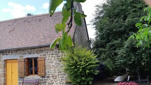 Un bâtiment en pierre avec un toit en tuiles, une porte en bois et un banc à l’extérieur.