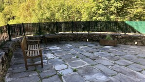 Un patio in pietra con una panchina di legno e un tavolo, circondato da un muro in pietra e un recinto verde.