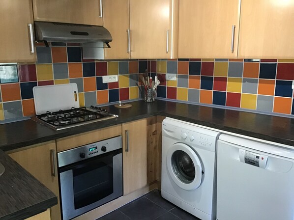 Una cocina con estufa a gas, horno, lavadora y un colorido salpicadero de azulejos.