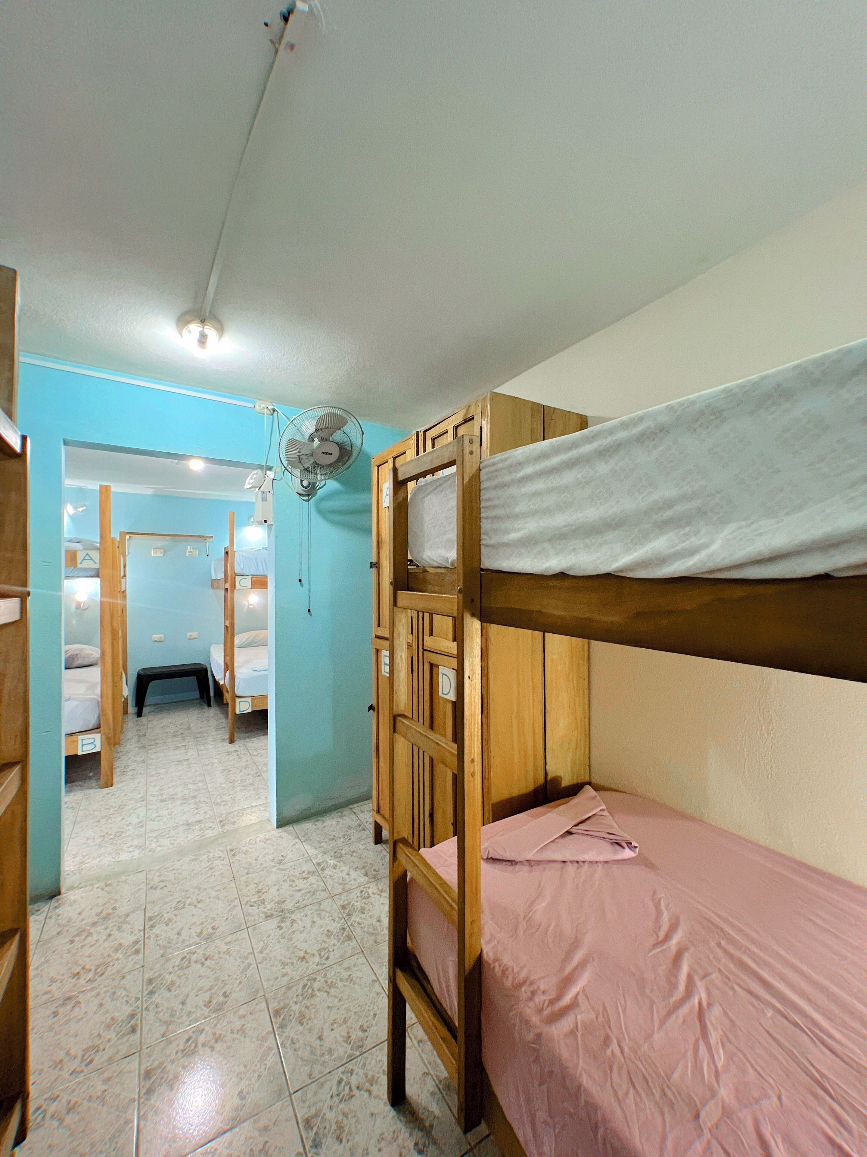 A dormitory room with bunk beds, a fan, and a tiled floor.