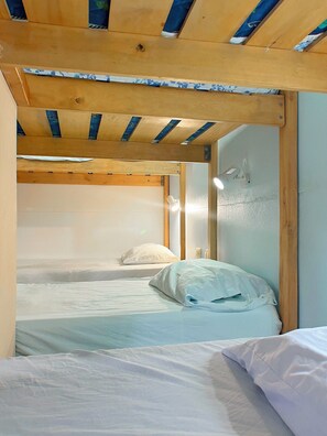 A bunk bed room with wooden beams and a single bed with white bedding. - Hostel Samara (Sámara)