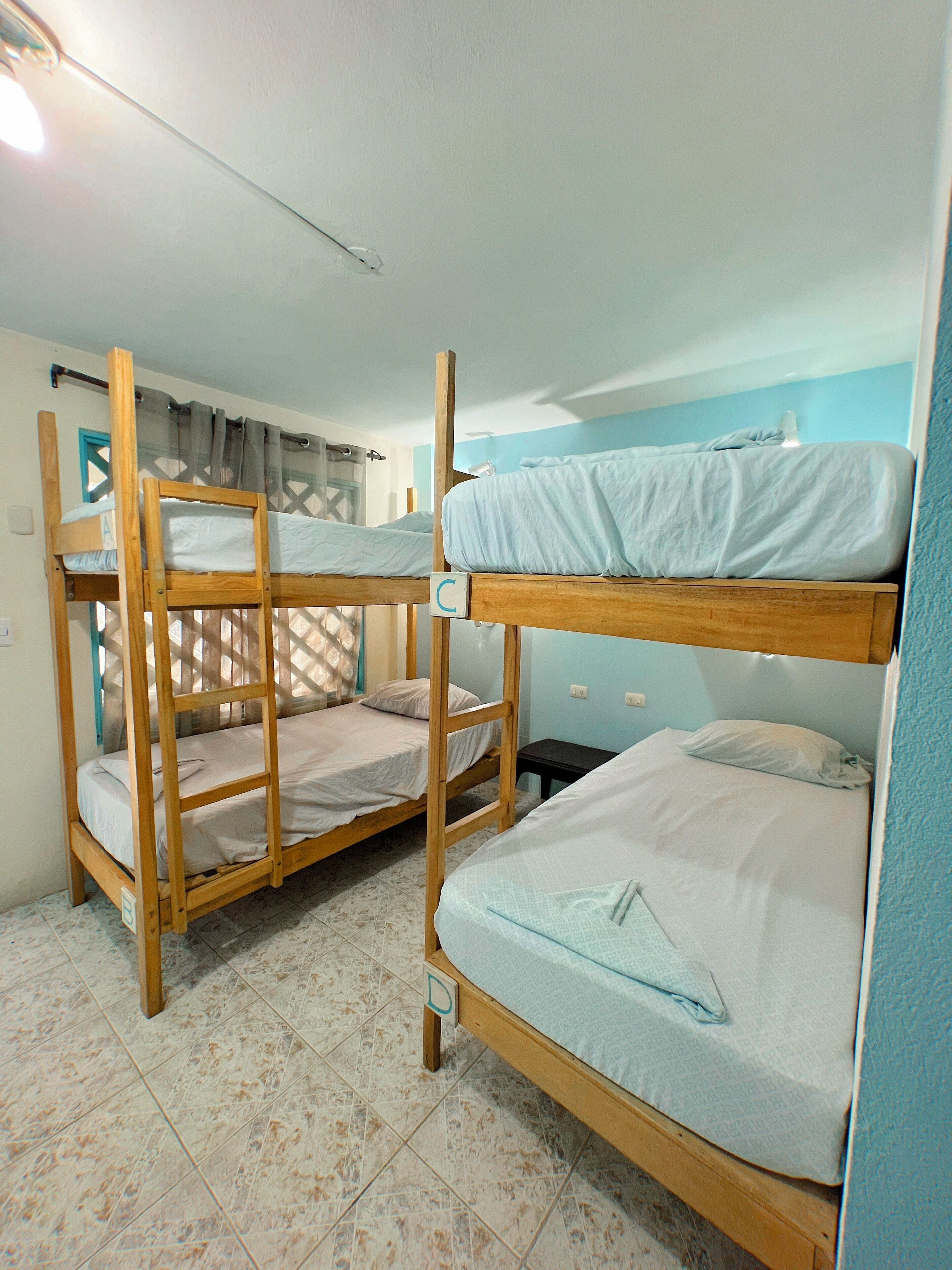 Une chambre avec des lits superposés, une fenêtre avec des rideaux et un sol carrelé.