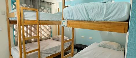 Une chambre avec des lits superposés, une fenêtre avec des rideaux et un sol carrelé.
