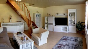 Un salon avec un escalier en bois, un canapé, une table basse, un téléviseur et une bibliothèque.