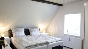 Une chambre avec un plafond en pente, une grande fenêtre, un lit recouvert d’une couvre-lit à motifs et des lampes de chevet.