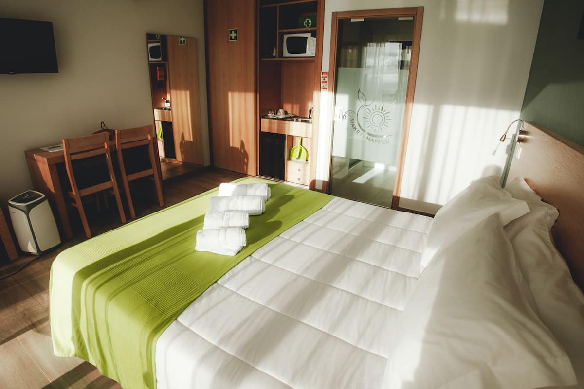 A hotel room with a bed, a desk, a chair, a wardrobe, and a bathroom.