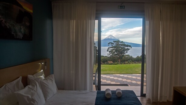 A hotel room with a bed, a view of a mountain and water, and a checkered outdoor area. - Make It Happen Farm (Velas)