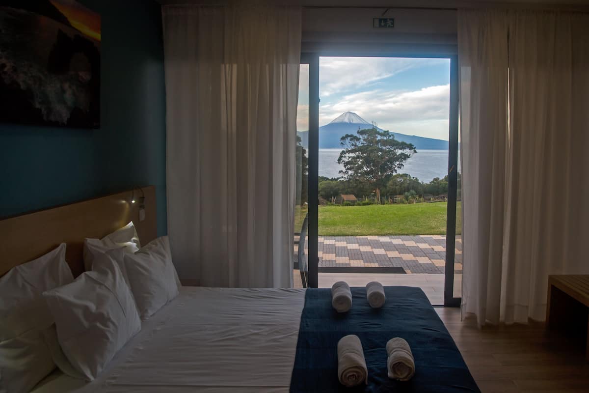 A hotel room with a bed, a view of a mountain and water, and a checkered outdoor area.