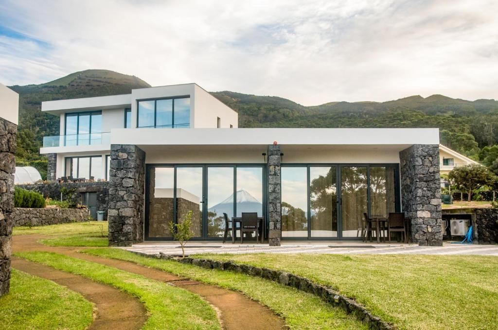 A modern two-story house with large glass windows, stone pillars, and a view of a mountain.