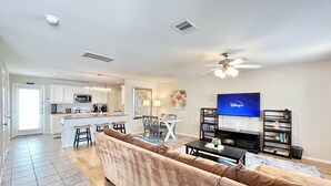 Un soggiorno moderno con un divano ampio, una televisione e una zona pranzo con cucina sullo sfondo.