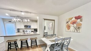 Una cucina moderna con mobili bianchi, elettrodomestici in acciaio inossidabile e un angolo bar. Si nota un tavolo da pranzo con quattro sedie e un tappeto sul pavimento.