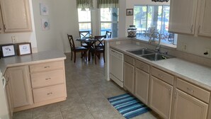 Una cocina con armarios de madera, lavavajillas, un fregadero y una zona de comedor con sillas y una mesa.