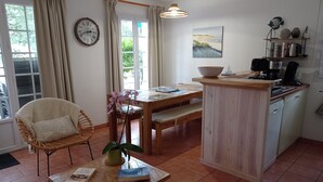 Eine gemütliche Küche mit Essbereich, ein Korbstuhl, ein Holztisch mit Büchern und Blick auf Grün hinter dem Fenster.