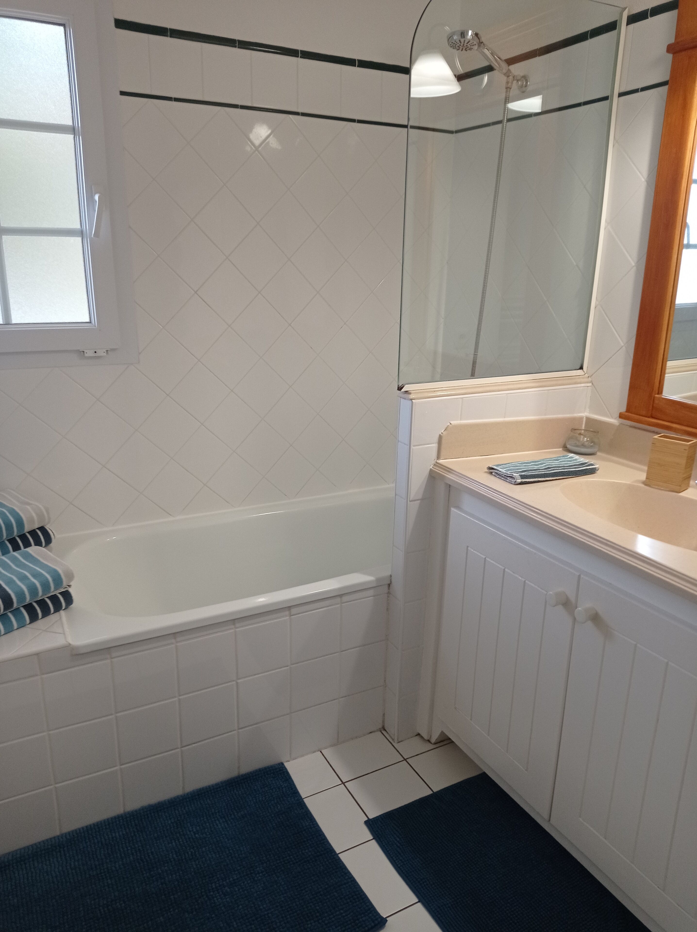 A bathroom with a white bathtub, a glass shower enclosure, a sink with a mirror, and a window.