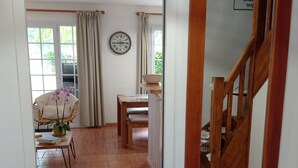 Ein Flur mit einer Holztreppe, einem Essbereich mit Tisch und Stühlen, einem Korbstuhl mit Pflanze und einer Wanduhr.