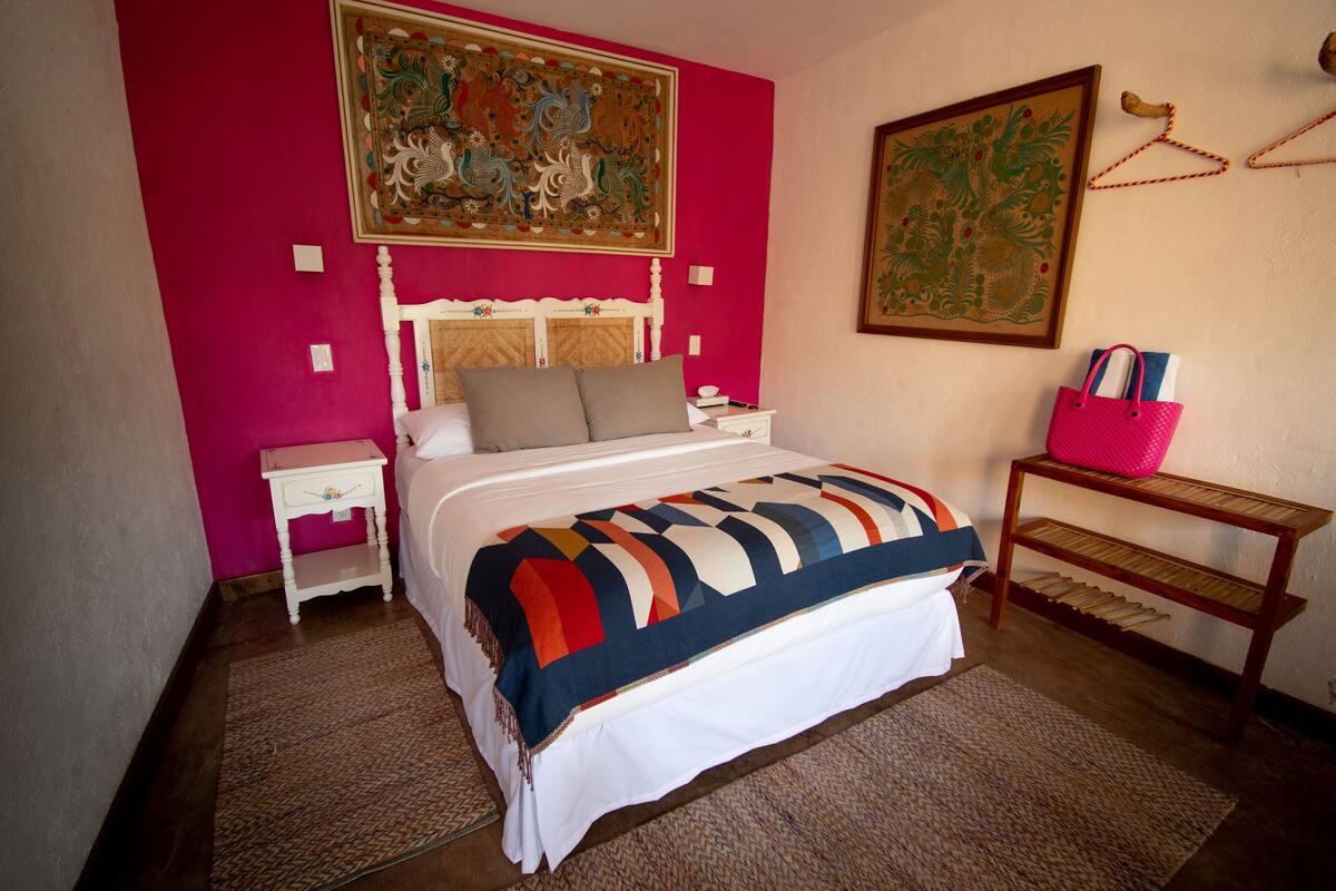 A bedroom with a bed, a nightstand, a wooden table, and two paintings on the wall.
