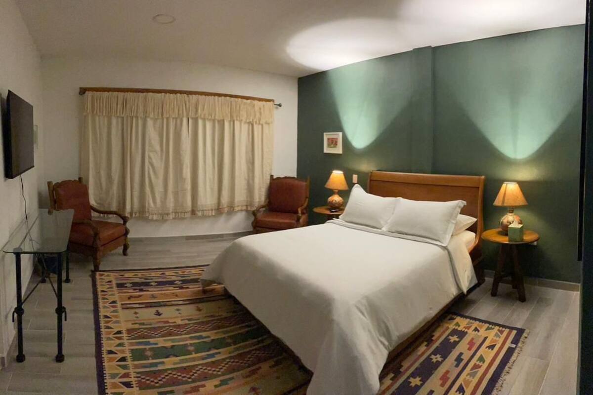 A hotel room with a bed, two chairs, a TV, and a lamp.
