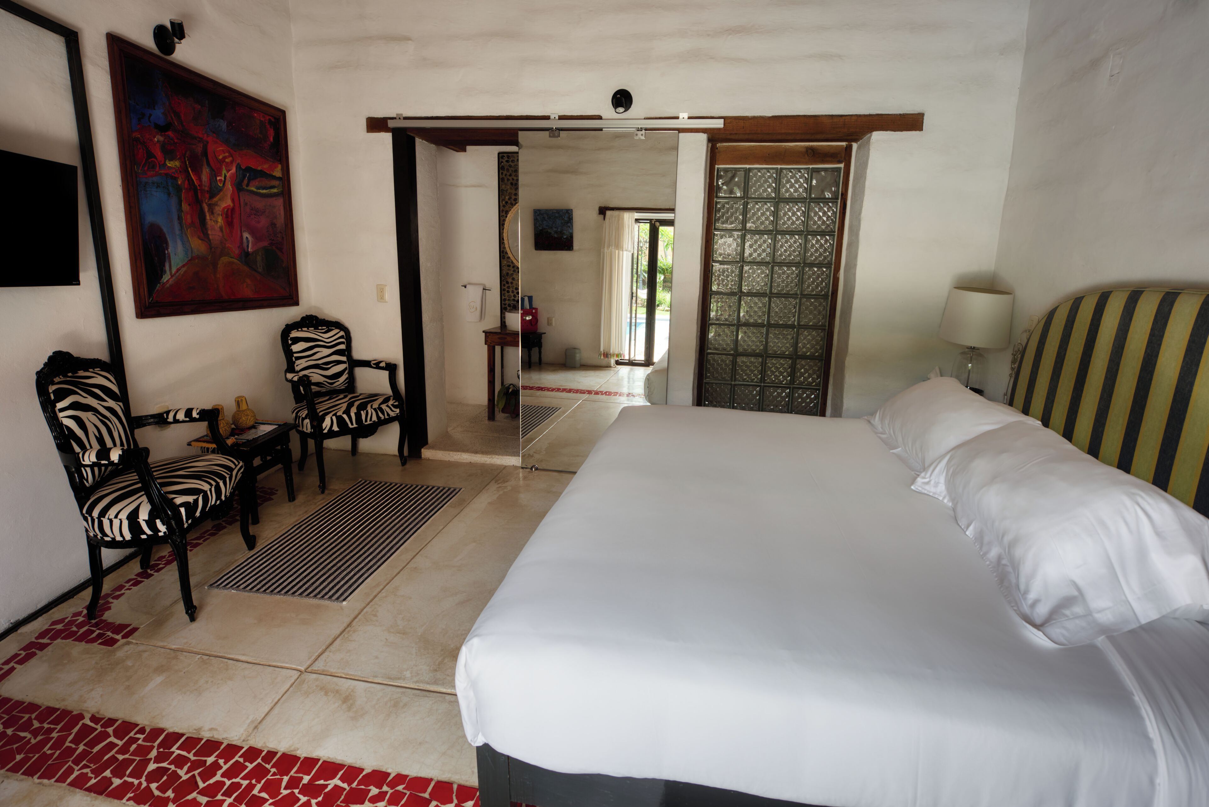 Habitación de hotel con una cama grande, dos sillas, un cuadro y vistas a través de una puerta abierta.