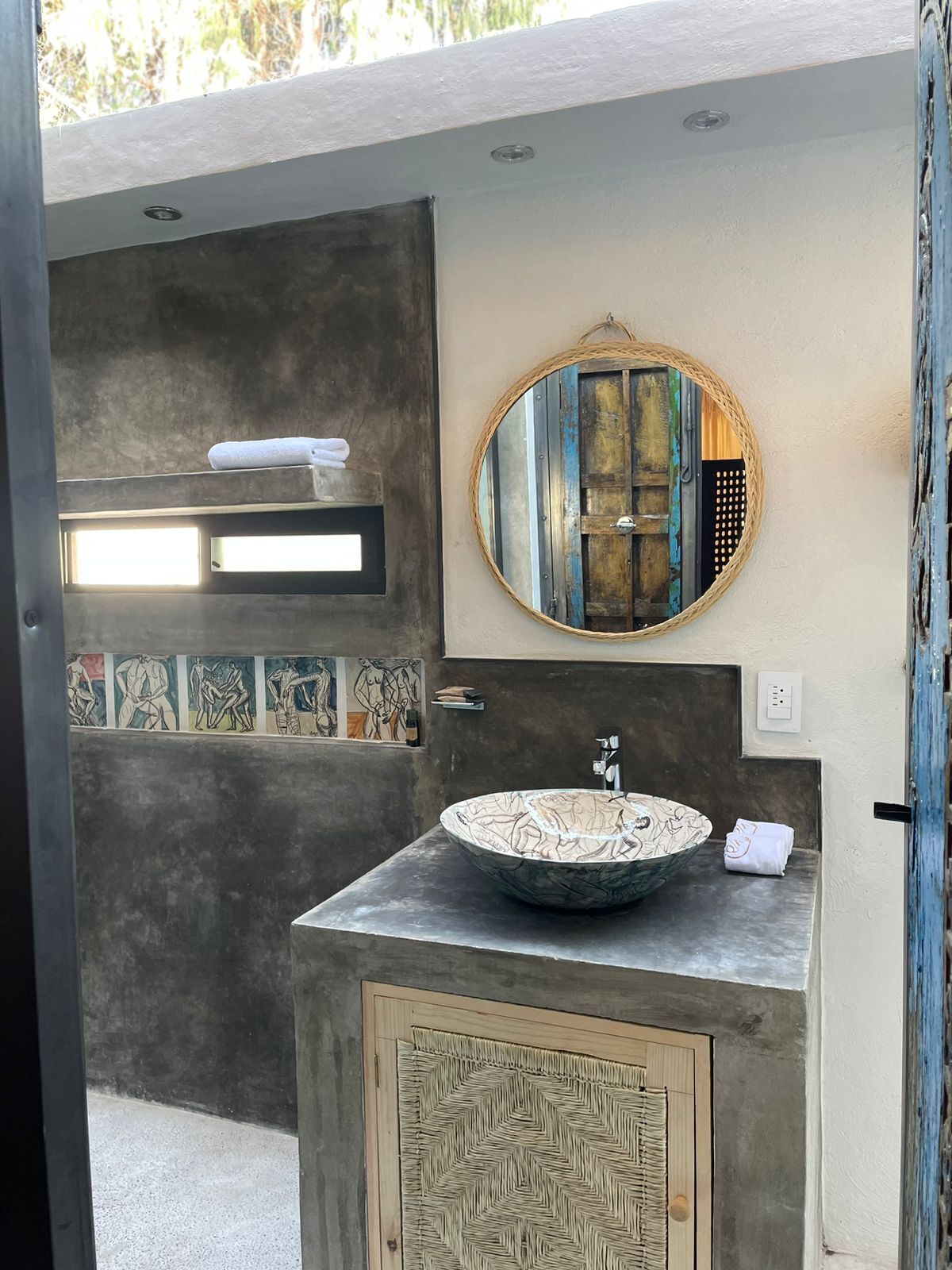 A modern bathroom with a large round mirror, a vessel sink, and a textured wall panel.