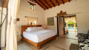 A bedroom with a wooden bed, a nightstand, a lamp, and a view of an outdoor swimming pool. - Quinta Ascension - Adults Only (Malinalco)