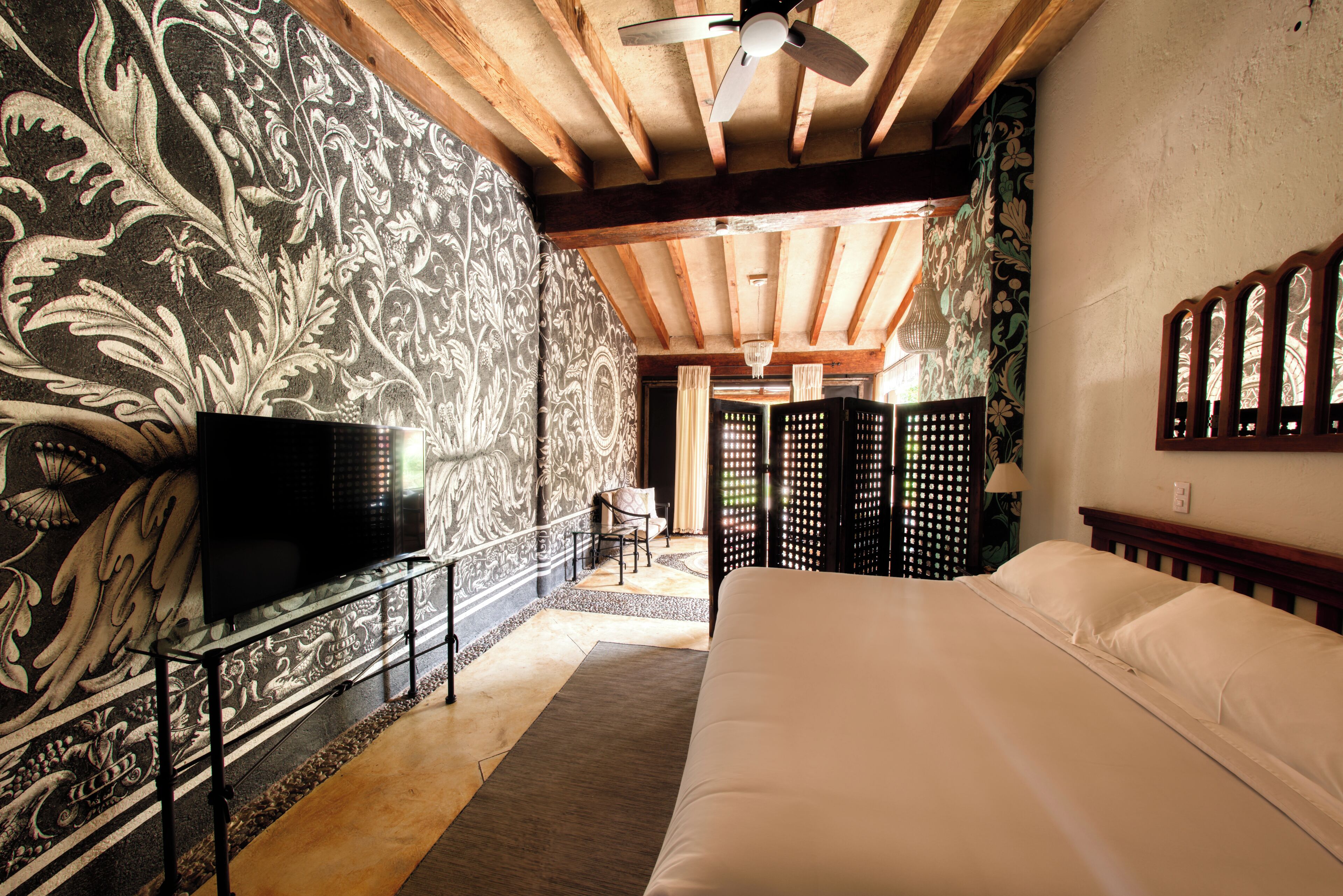 Un dormitorio con una cama grande, un televisor sobre un mueble, un ventilador de techo y una pared decorativa con estampado floral.
