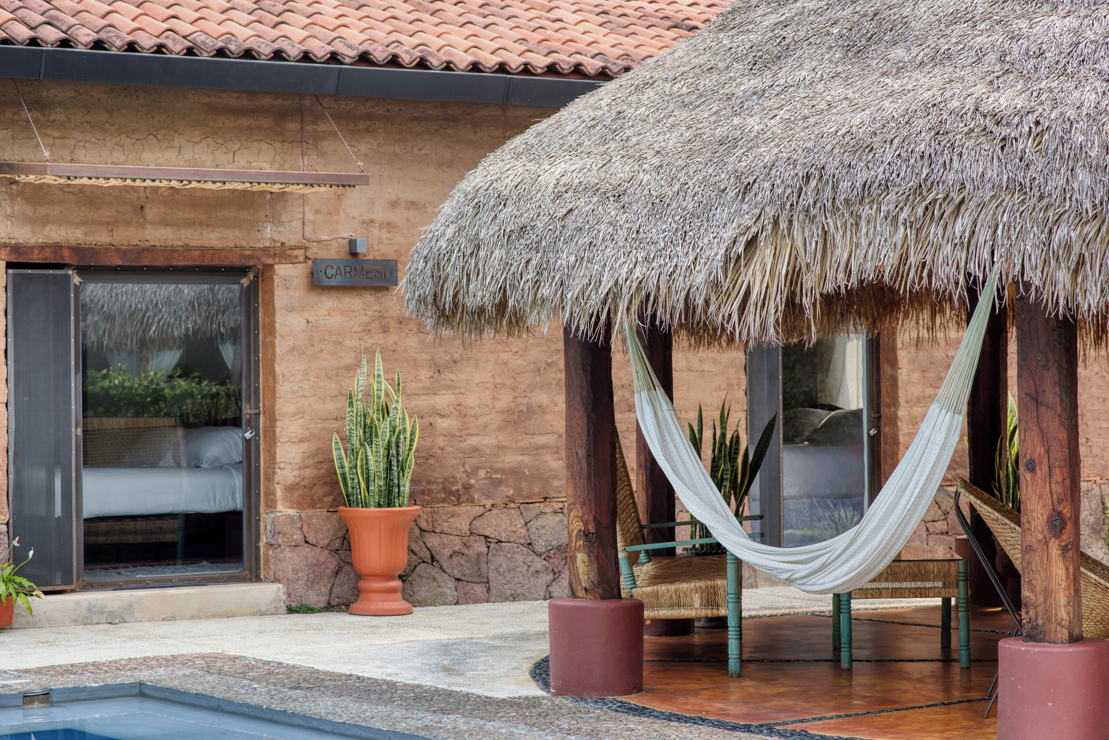 A building with a thatched roof, a pool, and a potted plant.