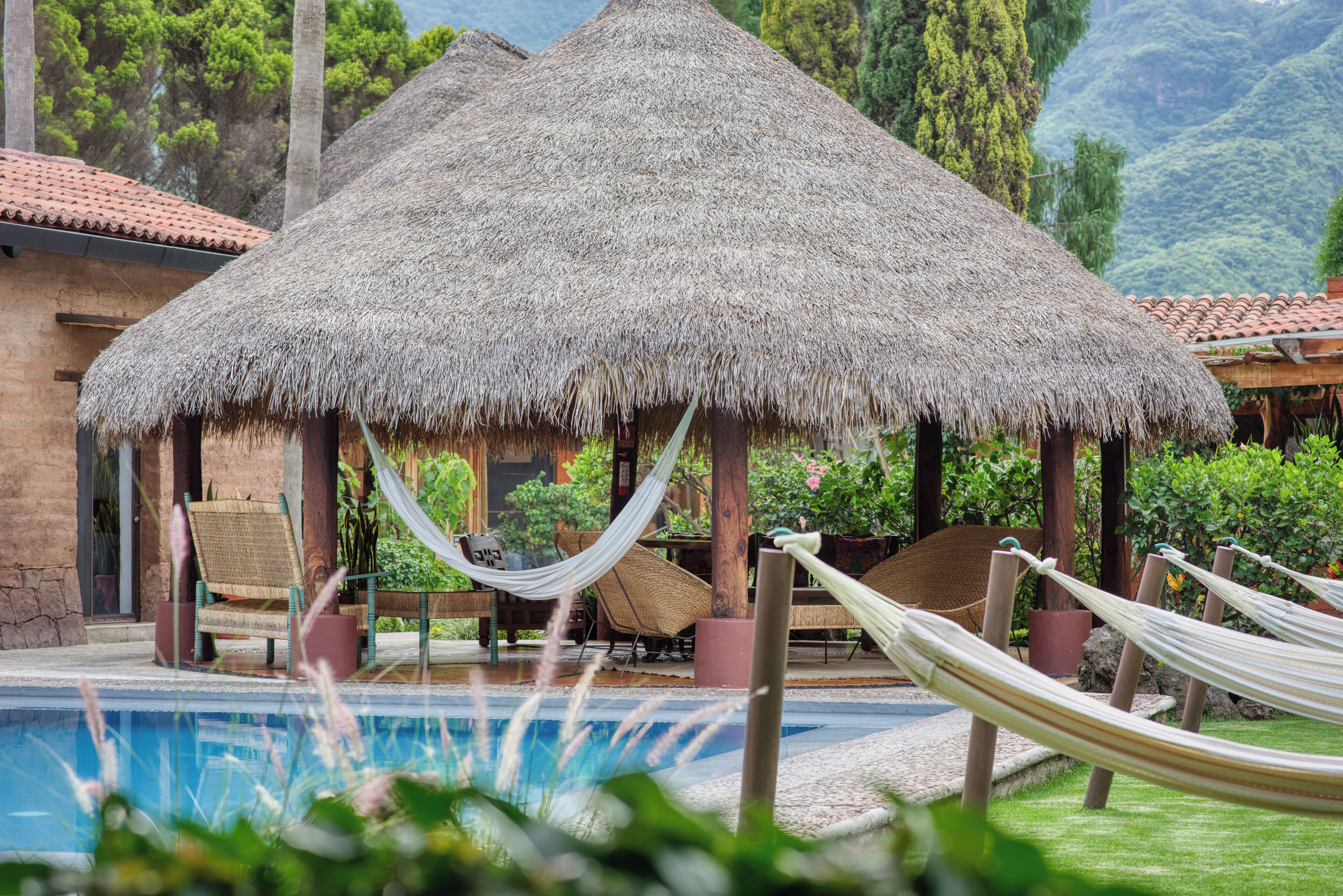 A thatched-roof structure with a pool and lounge chairs.