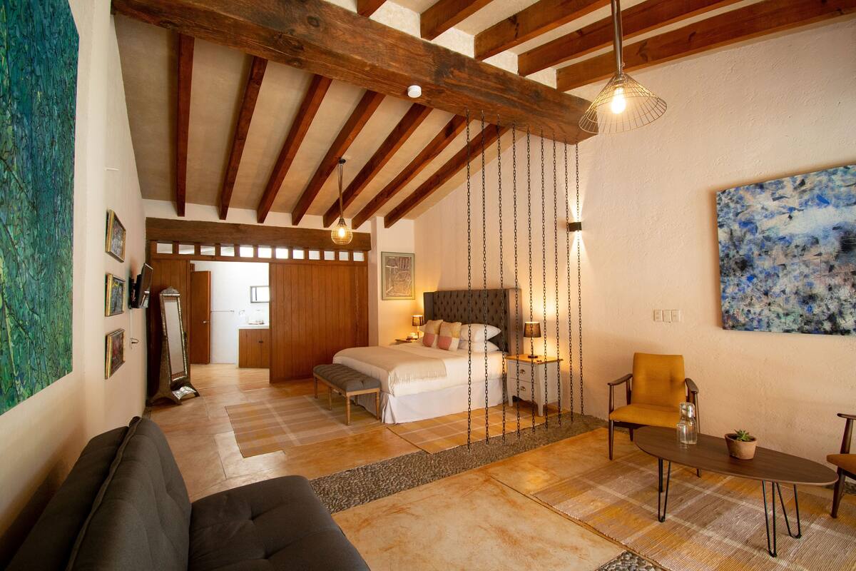 A bedroom with a bed, bedside table, chair, and a painting on the wall.