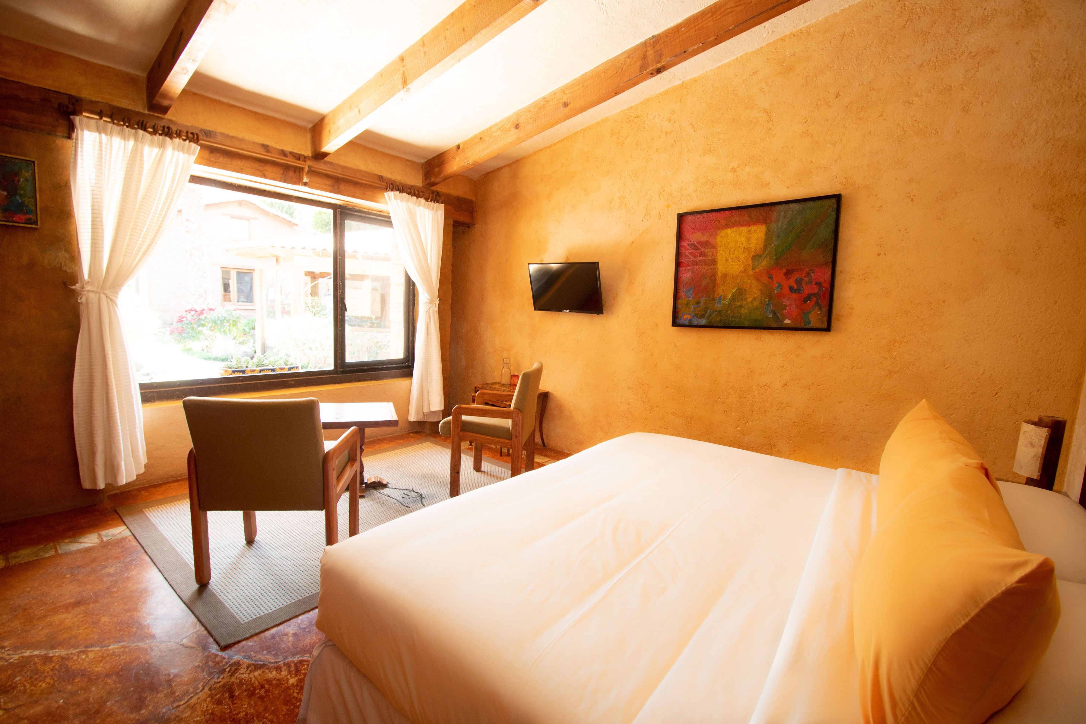 A hotel room with a bed, a desk, a chair, a TV, and a window with curtains.