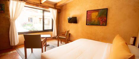 A hotel room with a bed, a desk, a chair, a TV, and a window with curtains.
