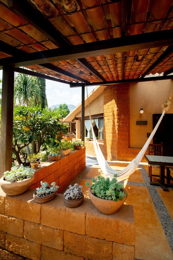 An outdoor patio with a hammock, potted plants, and a brick wall. - Quinta Ascension - Adults Only (Malinalco)