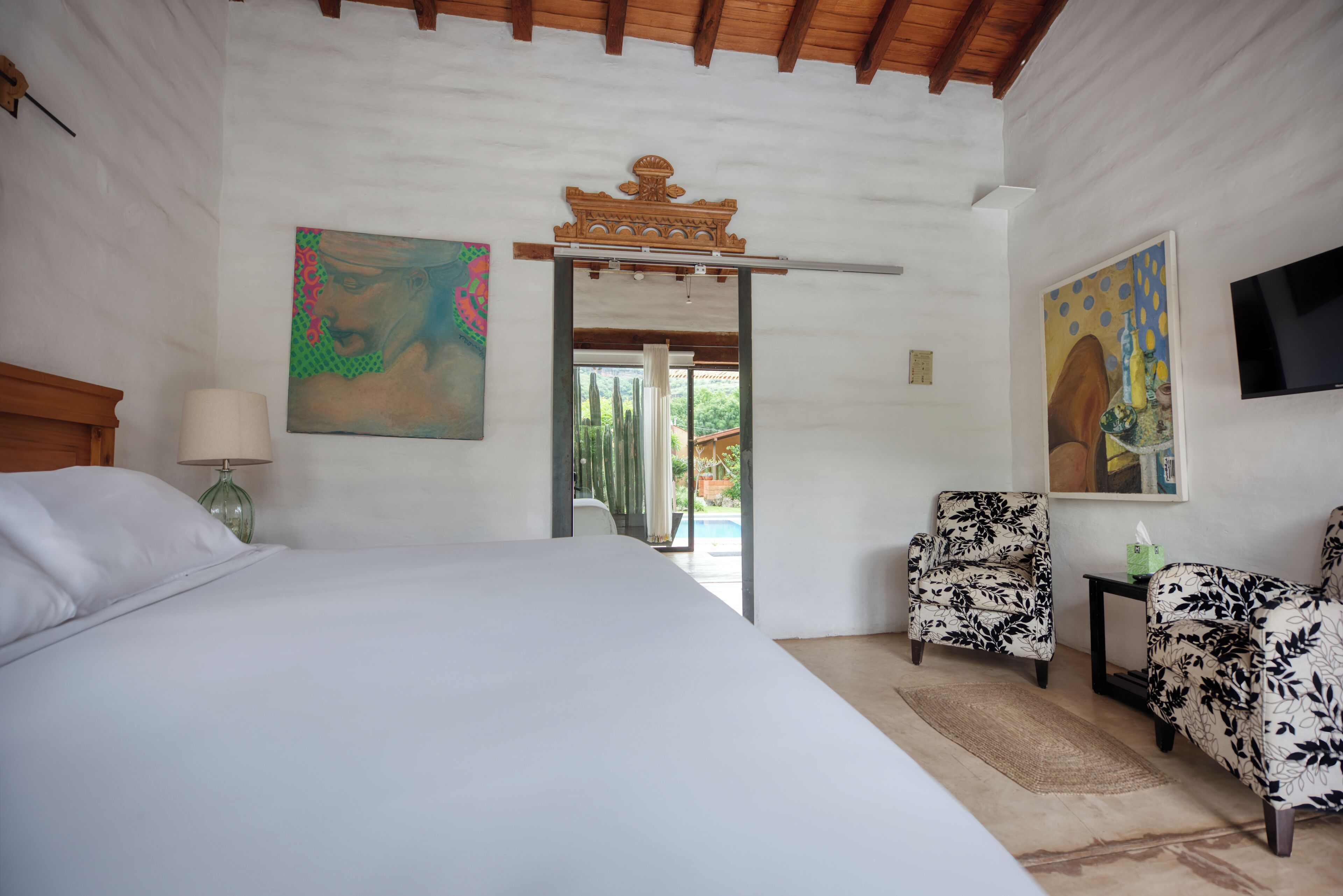A hotel room with a large bed, two armchairs, a TV, and artwork on the walls.