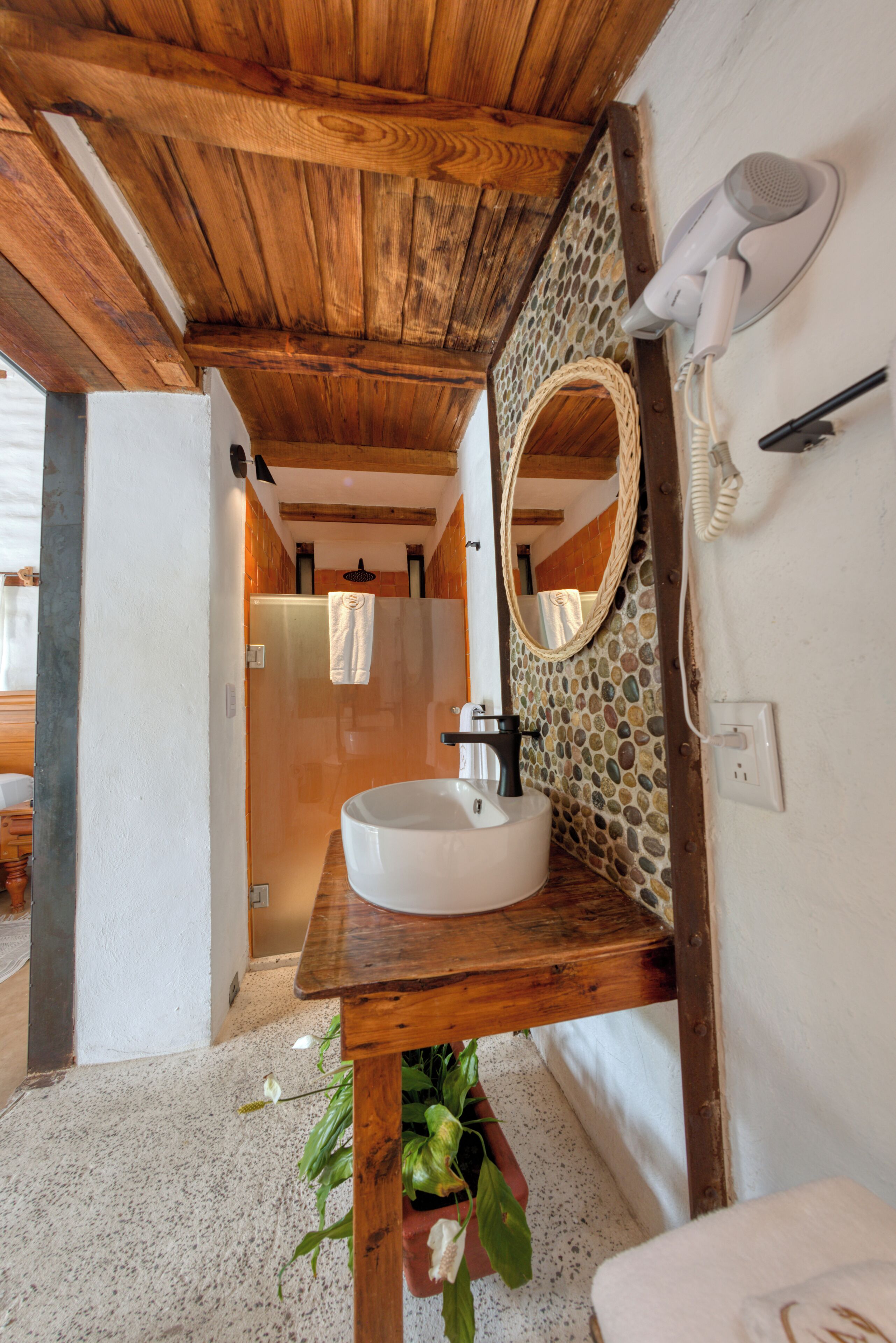 Une salle de bain avec un meuble-lavabo en bois, un miroir rond, un lavabo blanc et un espace douche.