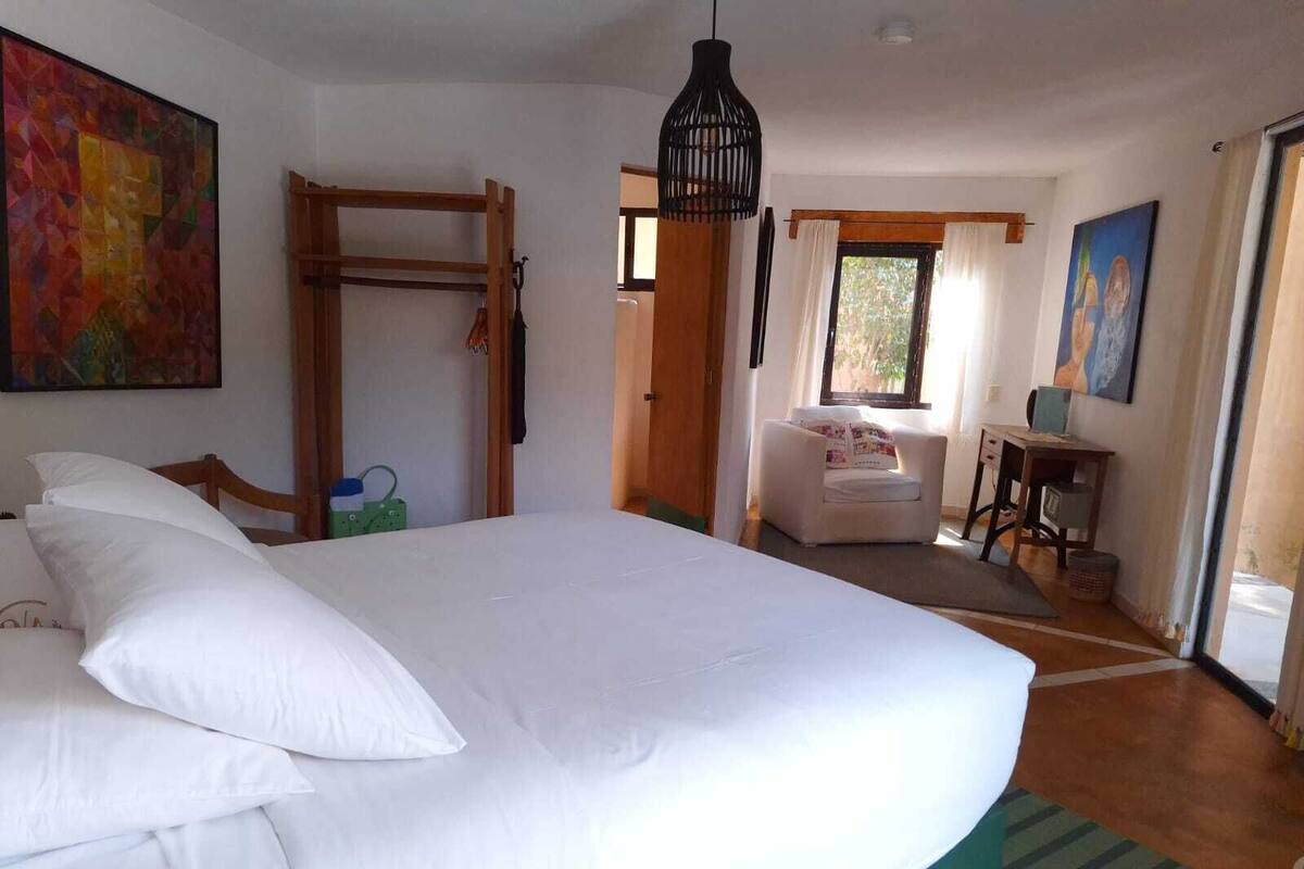A bedroom with a large bed, a wooden ladder, a desk, a chair, and a painting on the wall.