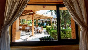 A view through a window with curtains, revealing an outdoor patio area with wooden furniture and a thatched roof structure. - Quinta Ascension - Adults Only (Malinalco)