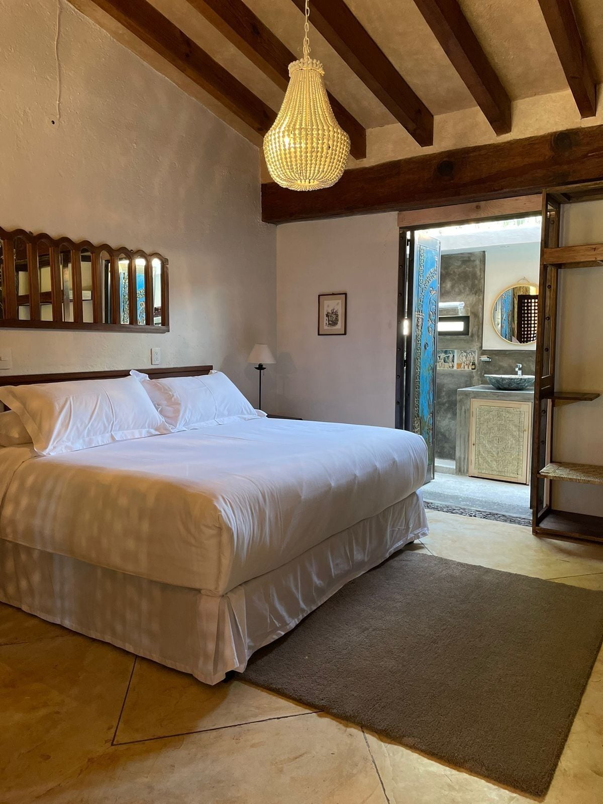 Een slaapkamer met een groot bed, een hanglamp, een houten plafond, een deur naar een badkamer en een klein vloerkleed.