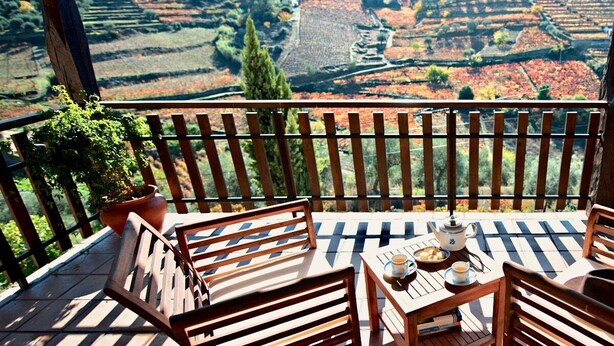 Une terrasse en bois avec une table et des chaises, donnant sur un vignoble en terrasses.