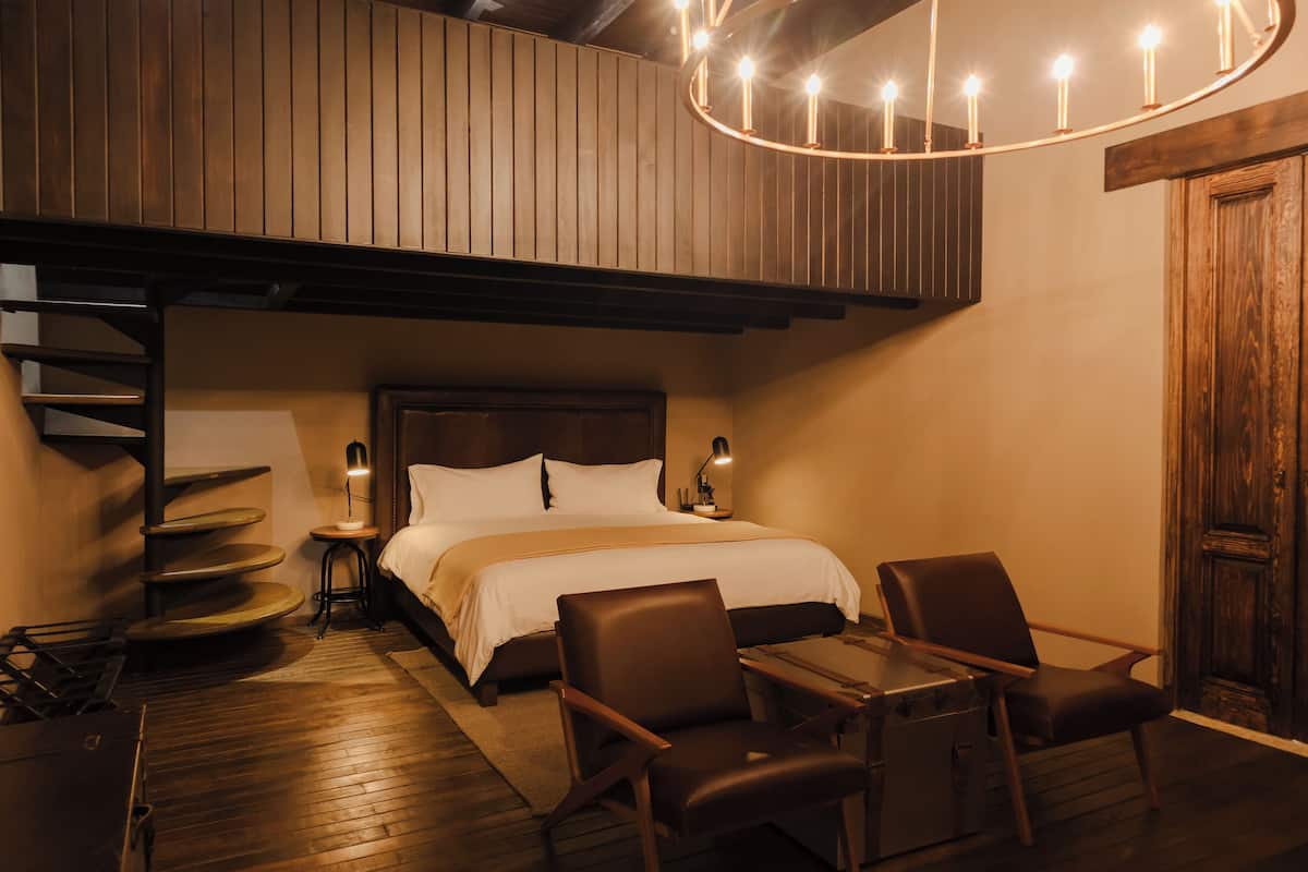 Ein Schlafzimmer mit einem Bett, zwei Stühlen, einem Tisch, einer Lampe und einer Holzbalkendecke.
