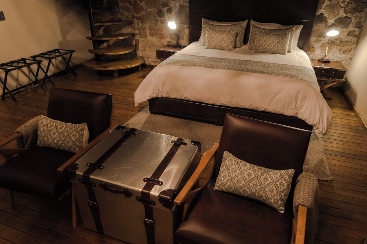 Ein gemütliches Zimmer mit einem großen Bett, zwei Sesseln, einem Holztisch und einem Koffer.