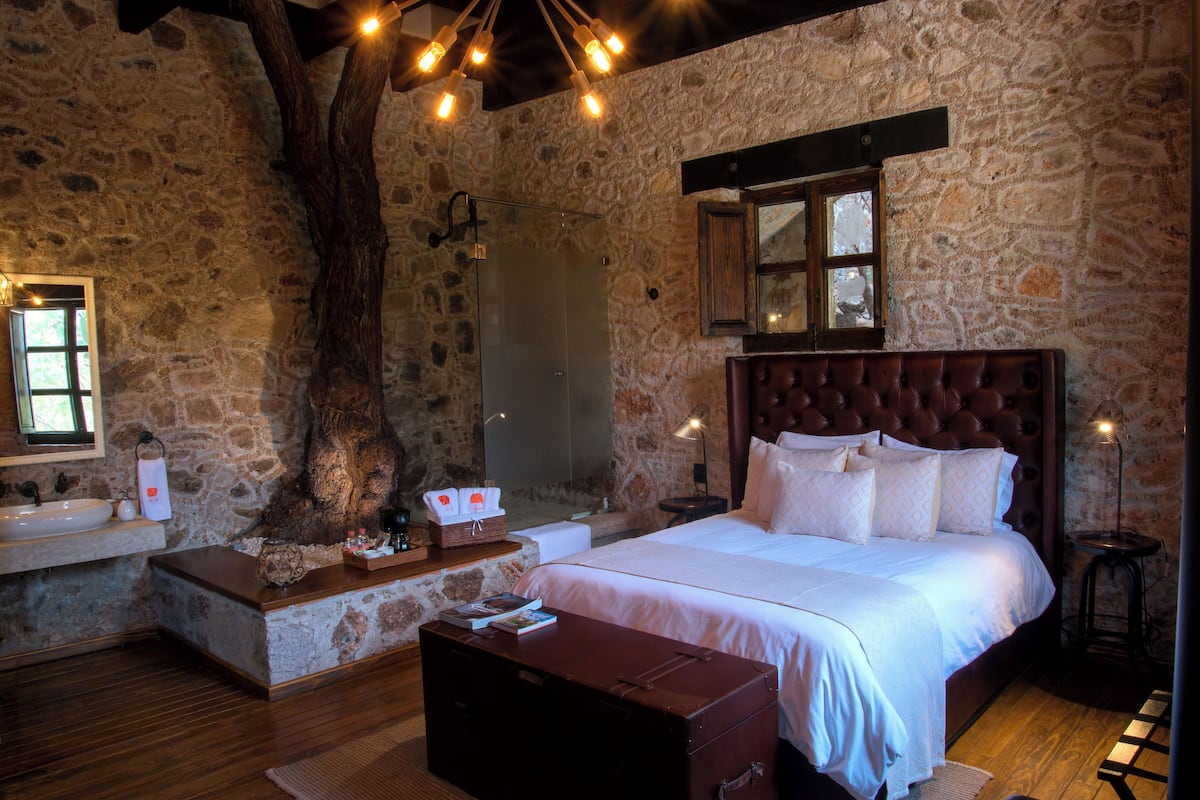 Ein Schlafzimmer mit Steinwänden, einem großen Bett, einer hölzernen Bank, einem Koffer und einer Steinsitzbank.