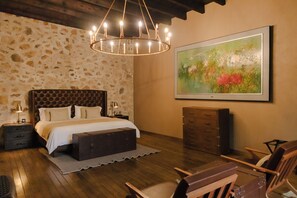 Ein Schlafzimmer mit einem großen Bett, Holzboden, einer Chandelier, einem Gemälde und einer Kommode.