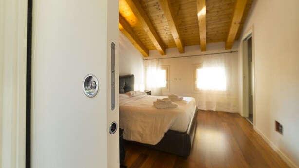 Un dormitorio con techo de madera, una cama con cubrecama blanco y una ventana con cortinas.