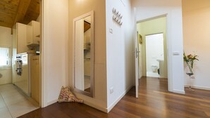 Un pasillo con suelo de madera, un espejo, una puerta que da a un baño y una planta pequeña.