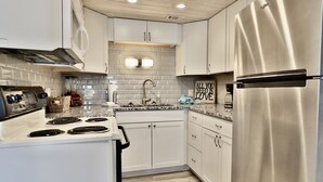 A modern kitchen with white cabinets, a stainless steel refrigerator, a built-in oven, and a granite countertop.