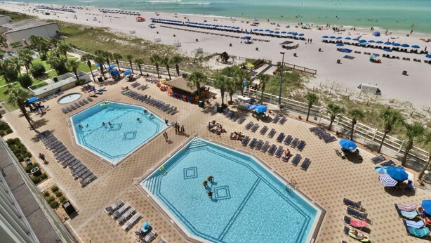 A resort with two large swimming pools, a beach area, and a view of the ocean.
